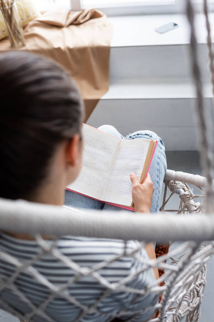 Asılı koltukta oturmuş kitap okuyan genç bir kadının arka plan görüntüsü  - Fotoğraf, Görsel