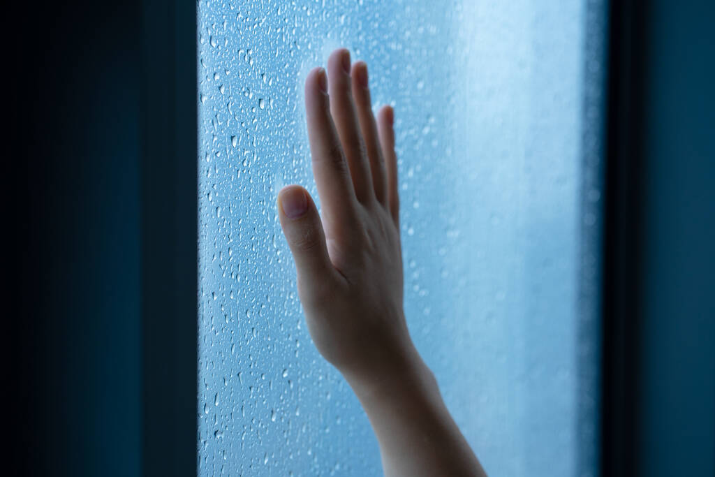 Mano femenina en la ventana durante la lluvia. Vidrio en gotas de agua - Foto, Imagen