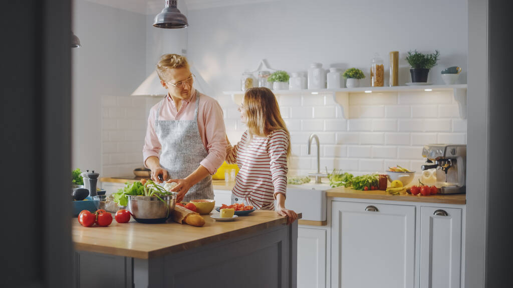Handsome Young Man in Glasses Wearing Apron and Beautiful Girl are Preparing a Salad in the Kitchen. Happy Couple are Hugging Each Other. Natural Clean Diet and Healthy Way of Life Concept. - Photo, Image