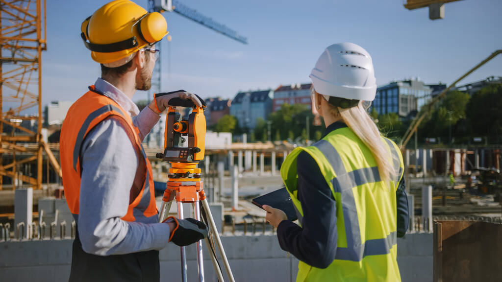 Construction Worker Using Theodolite Surveying Optical Instrument for Measuring Angles in Horizontal and Vertical Planes on Construction Site. Engineer and Architect Using Tablet Next to Surveyor. - Photo, Image