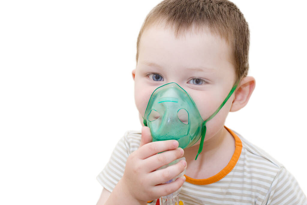 Mały niebieskooki chłopiec z bliska na białym tle z maską z inhalatora na twarzy, trzymający ją ręką. Poziome zdjęcie. Koncepcja - leczenie chorób układu oddechowego, zapalenie oskrzeli. - Zdjęcie, obraz