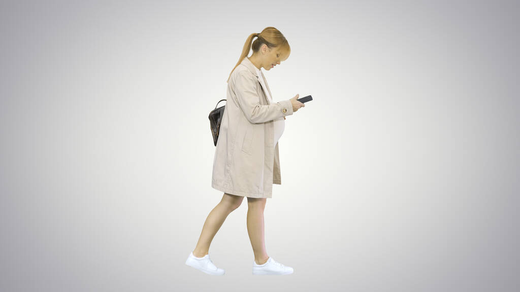 Elinde telefon olan hamile bir kız gradyan arka planda yürüyor. - Fotoğraf, Görsel