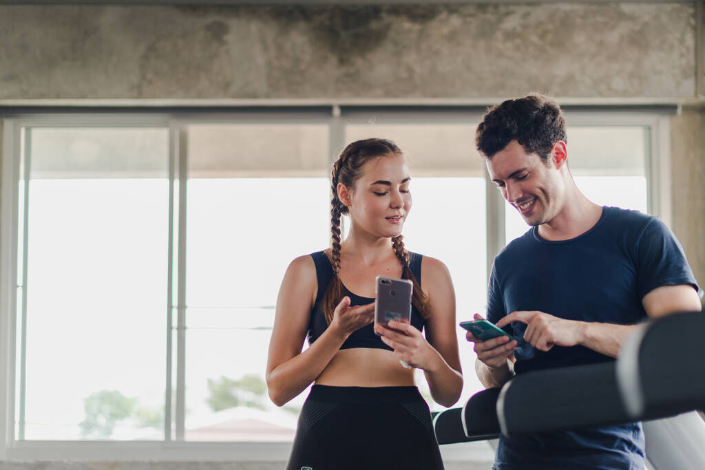 Paare turnen im Fitnessstudio. Paar hat Spaß beim Spielen mit Smartphones neben dem Trainingsgerät. - Foto, Bild