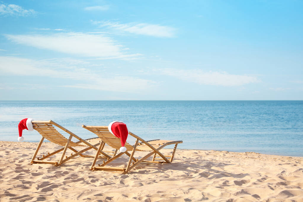 Сонячні шезлонги з капелюхами Санти на пляжі, місце для тексту. Різдвяні канікули
 - Фото, зображення