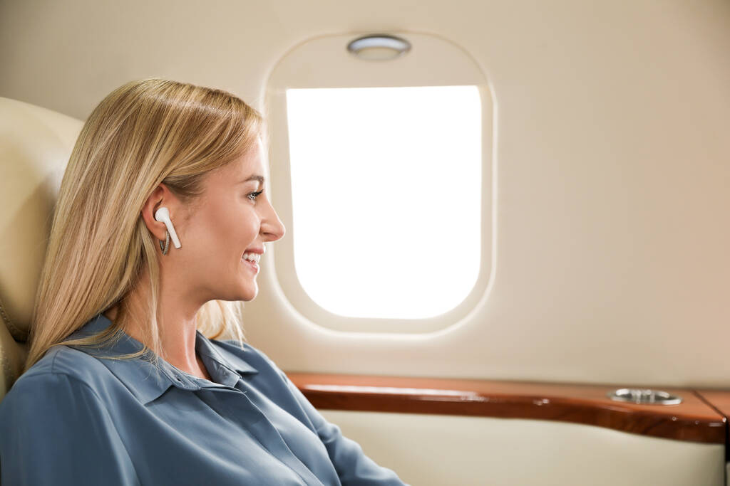 Красивая женщина слушает музыку через беспроводные наушники во время полета. Авиаперелеты - Фото, изображение