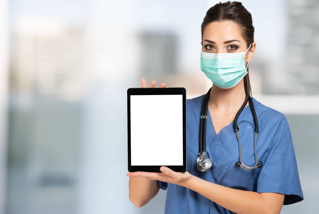 Medico infermiere mascherato che mostra una compressa con schermo bianco - Foto, immagini