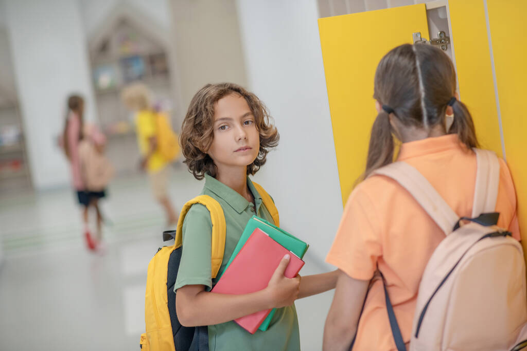Koyu saçlı çocuk okul koridorunda sınıf arkadaşıyla konuşuyor. - Fotoğraf, Görsel