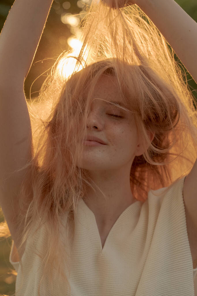 Portrait extérieur de jolie jeune femme blonde en pull tricoté blanc regardant la caméra avec un sourire joyeux, matin lever de soleil arrière-plan - Photo, image