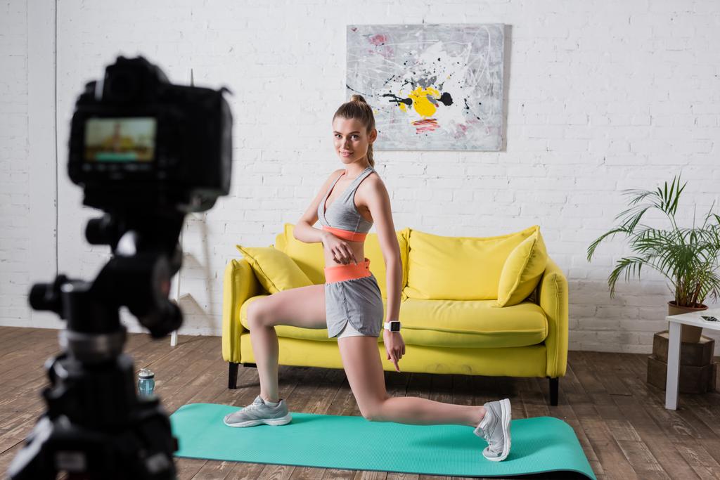 Foco seletivo da esportista se exercitando no tapete de fitness perto da câmera digital em casa  - Foto, Imagem