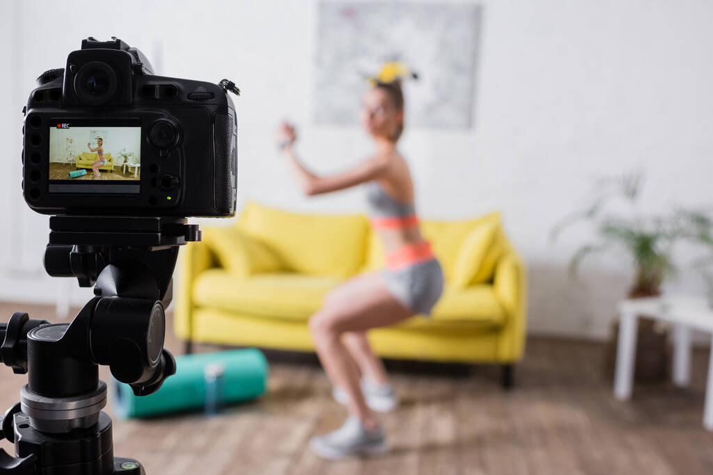 Selectieve focus van jonge sportvrouw training in de buurt van digitale camera in woonkamer  - Foto, afbeelding