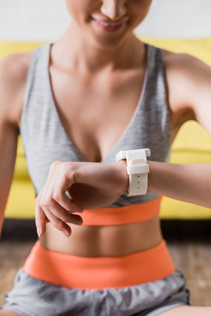 Cropped view of smiling sportswoman with smartwatch at home  - Photo, Image