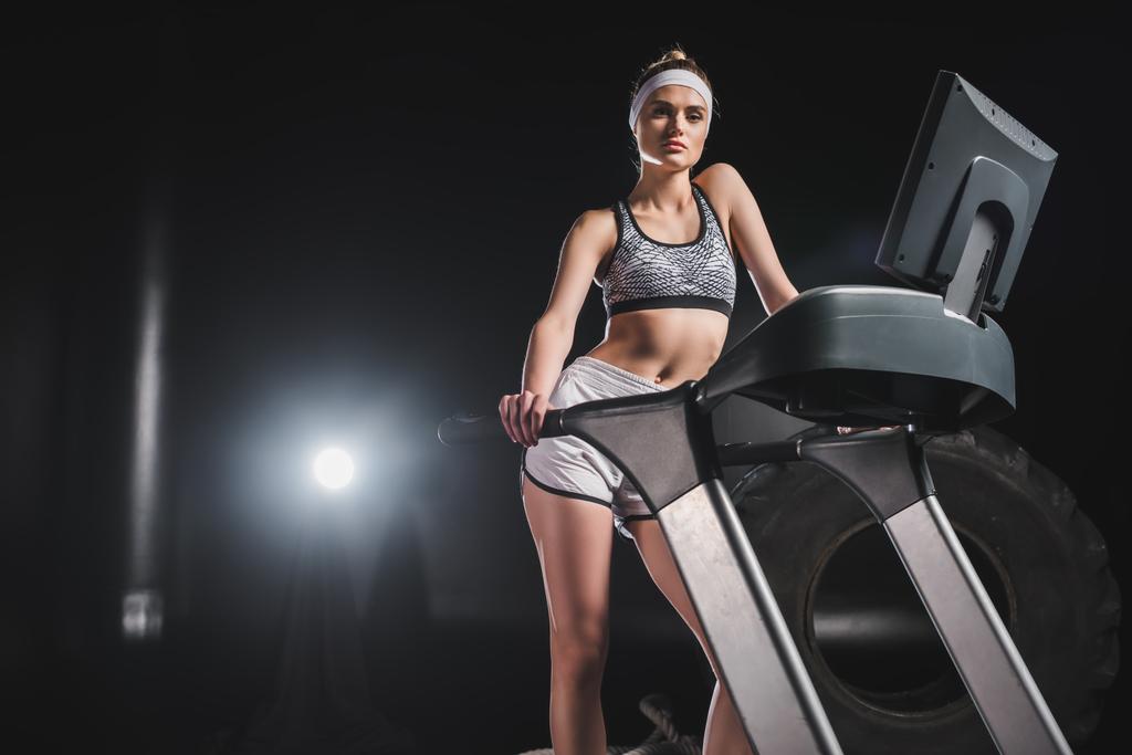 Sportswoman looking at camera while standing on treadmill in gym  - Photo, Image