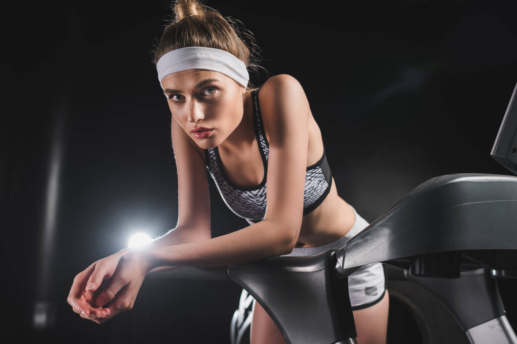 Fiatal sportos nő fejpántban nézi a kamerát a futópadon a sportközpontban  - Fotó, kép