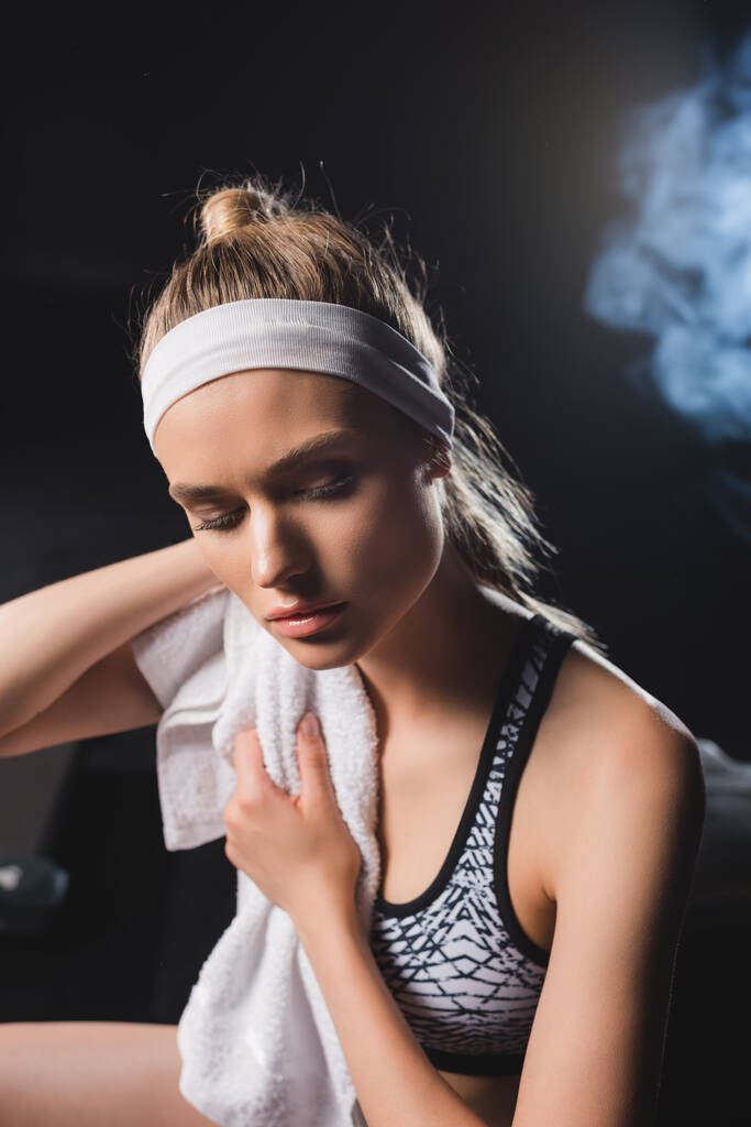 Selective focus of young sportswoman holding towel in gym with smoke  - Photo, Image