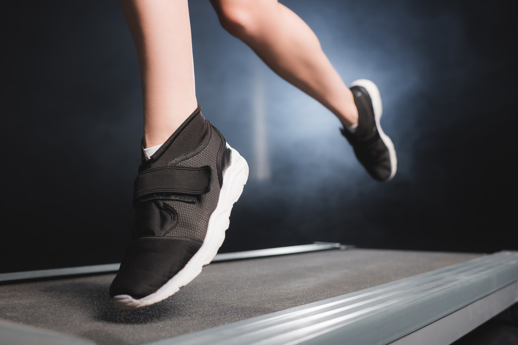 Vista recortada de la deportista en zapatillas de entrenamiento en la cinta de correr en el gimnasio con humo   - Foto, imagen