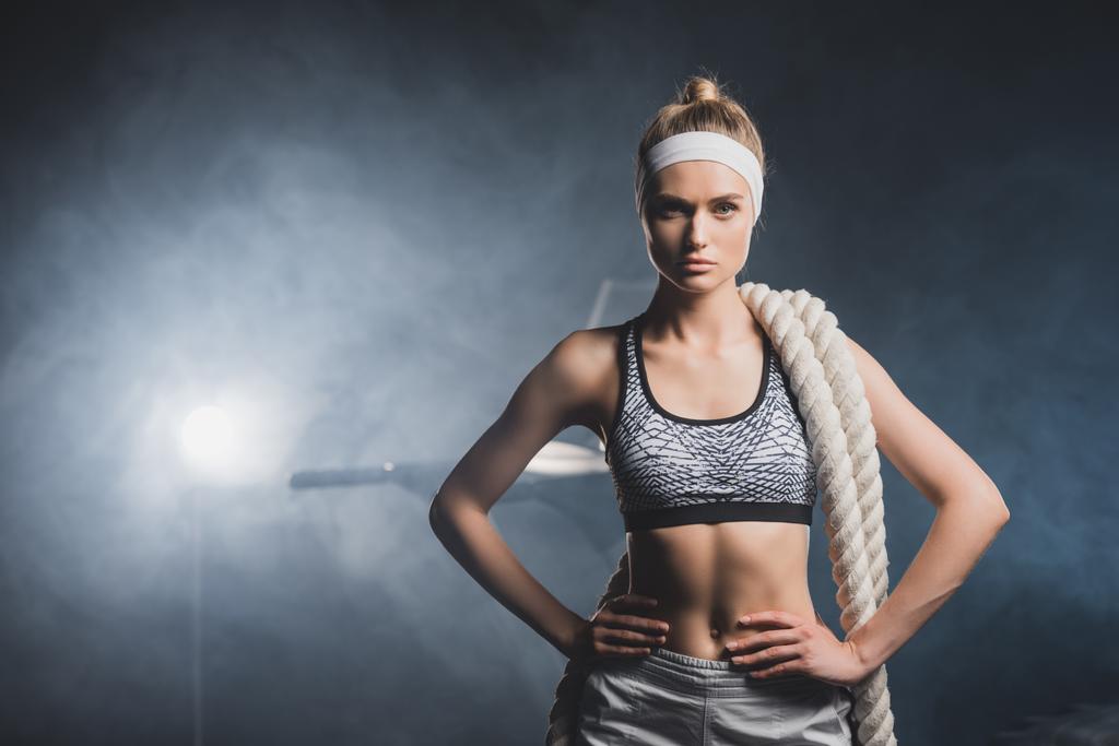 Αθλητική γυναίκα σε κορδέλα με σχοινί μάχης κοιτάζοντας κάμερα στο γυμναστήριο με καπνό  - Φωτογραφία, εικόνα