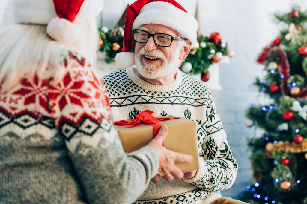 Selektiver Fokus der Seniorin überreicht Geschenkbox an fröhlichen Ehemann - Foto, Bild