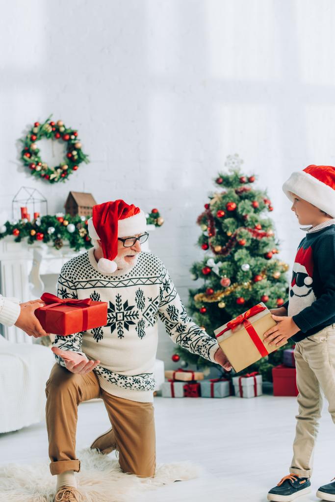 grand-père dans le chapeau de père Noël prendre des cadeaux de petits-enfants sur Noël - Photo, image