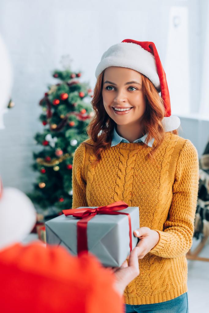 selective focus of happy woman in santa hat taking gift box from husband - Photo, Image