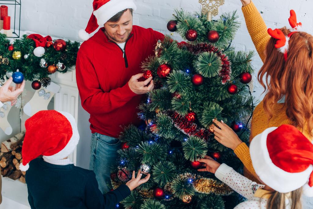 サンタの帽子の幸せな家族一緒に家でクリスマスツリーを飾る - 写真・画像