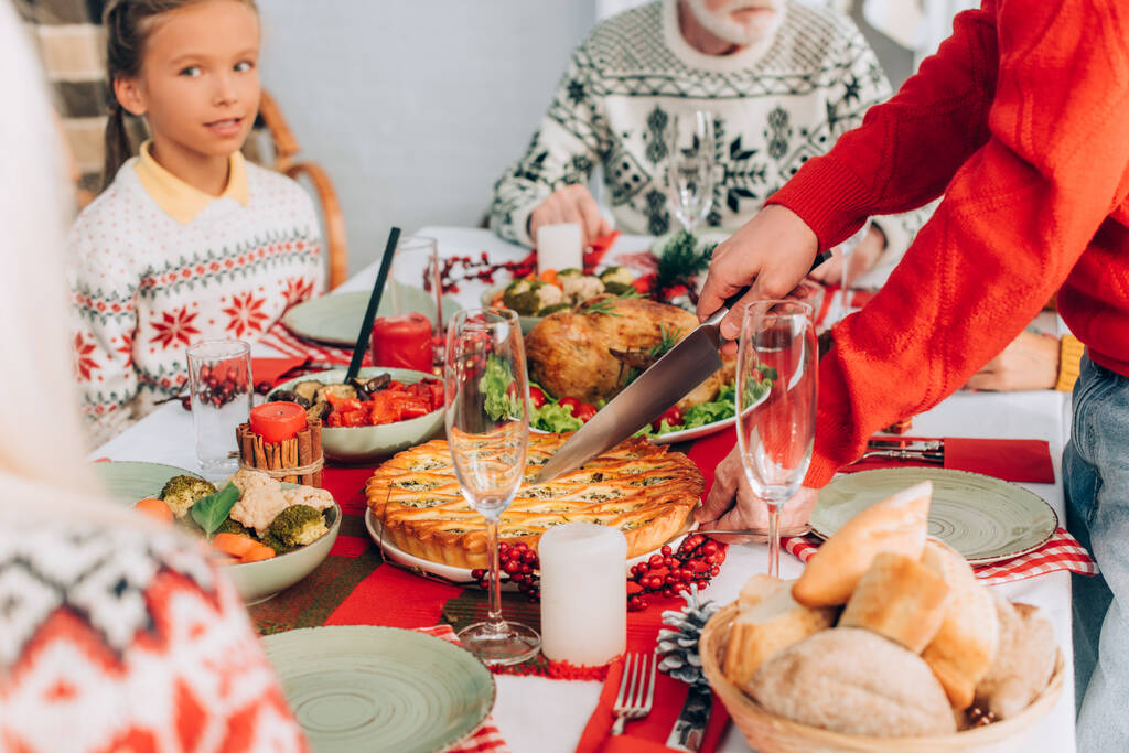 Focus selettivo di uomo torta di taglio sul tavolo festivo vicino alla famiglia a casa - Foto, immagini