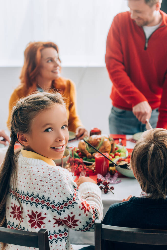Selective focus of girl looking at camera, sitting at festive table with family - Photo, Image