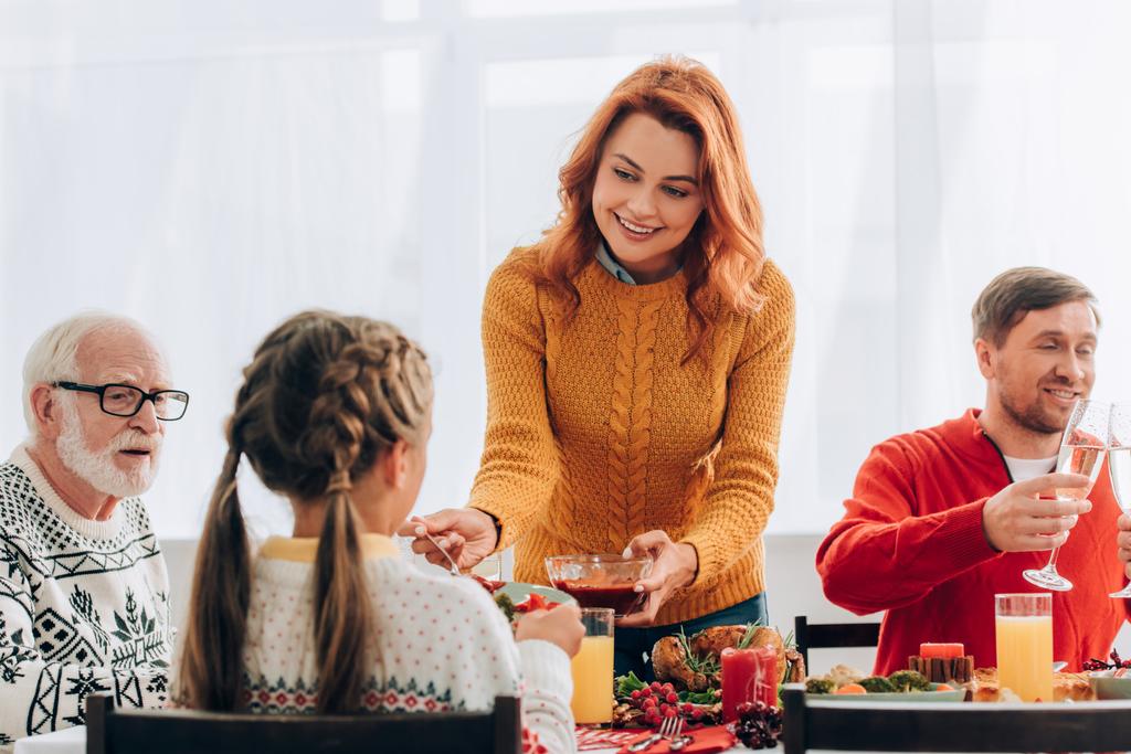 Donna rossa che serve salsa sul piatto vicino alla famiglia al tavolo festivo - Foto, immagini