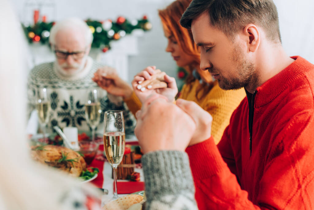 Foco seletivo do homem de mãos dadas com a família enquanto está sentado na mesa festiva - Foto, Imagem