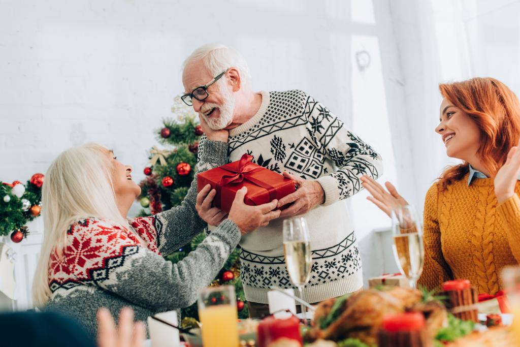 Smiling grandfather greeting wife with present near family applauding at home - Photo, Image