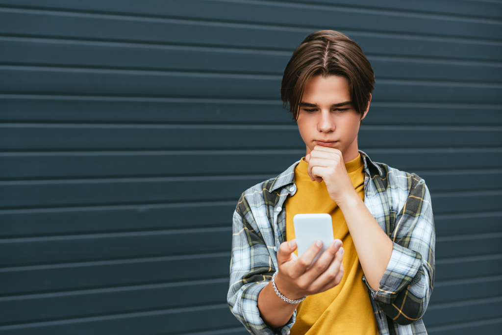 Adolescente pensativo usando smartphone perto de construção ao ar livre  - Foto, Imagem