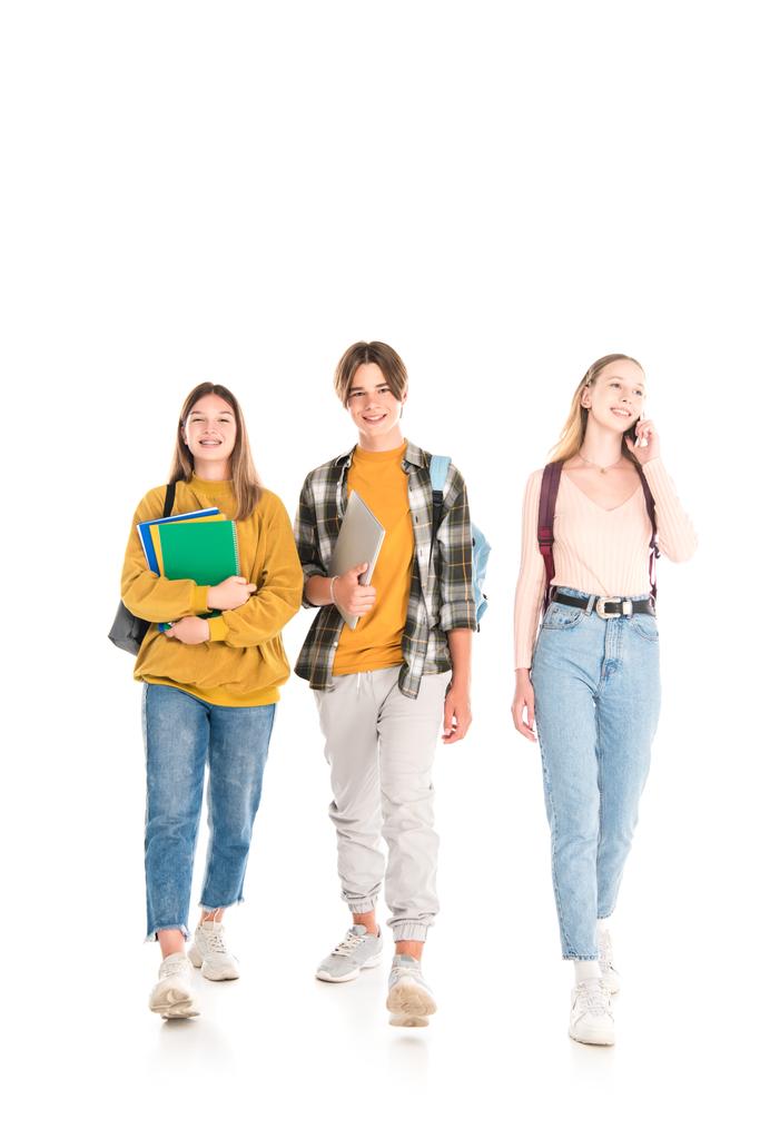 Adolescentes sonrientes con mochilas, cuadernos y teléfonos inteligentes caminando sobre fondo blanco - Foto, imagen