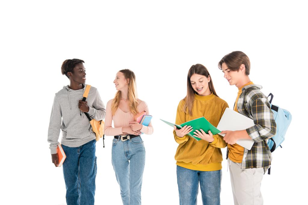 Усміхнені багатоетнічні підлітки з ноутбуком і блокнотами розмовляють ізольовано на білому
 - Фото, зображення