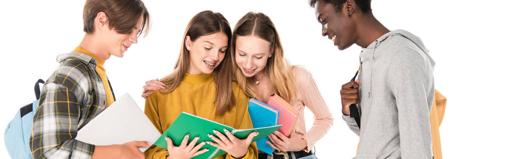 Заголовок сайта улыбающихся мультиэтнических подростков, смотрящих на блокнот, изолированный на белом - Фото, изображение