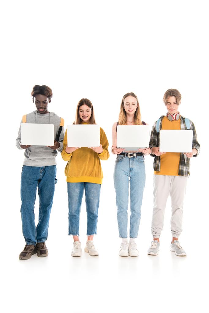 Улыбающиеся многонациональные подростки с рюкзаками, держащие ноутбуки на белом фоне - Фото, изображение