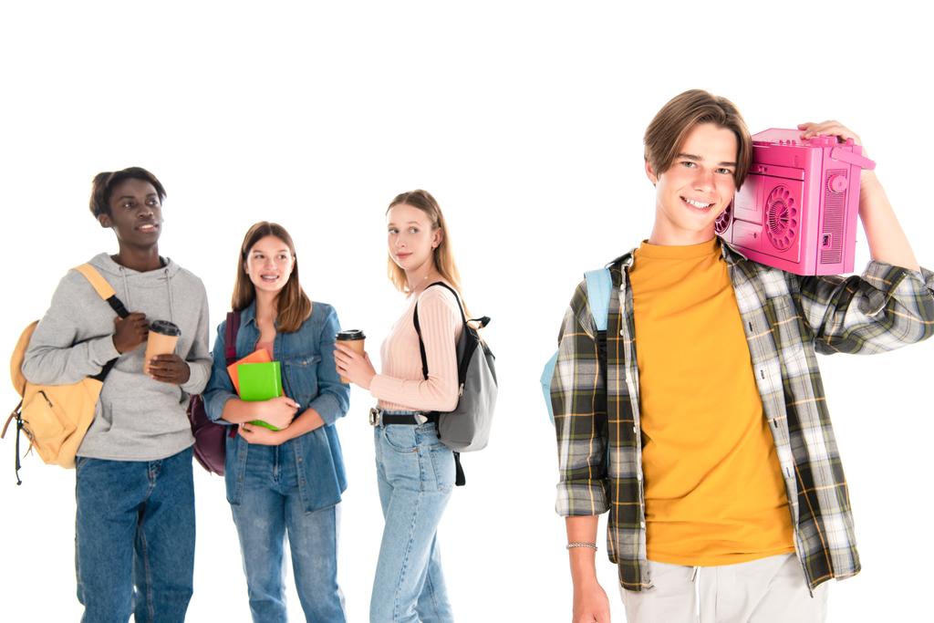 Usmívající se teenager drží boombox v blízkosti multietnických přátel s kávou jít a knihy izolované na bílém - Fotografie, Obrázek