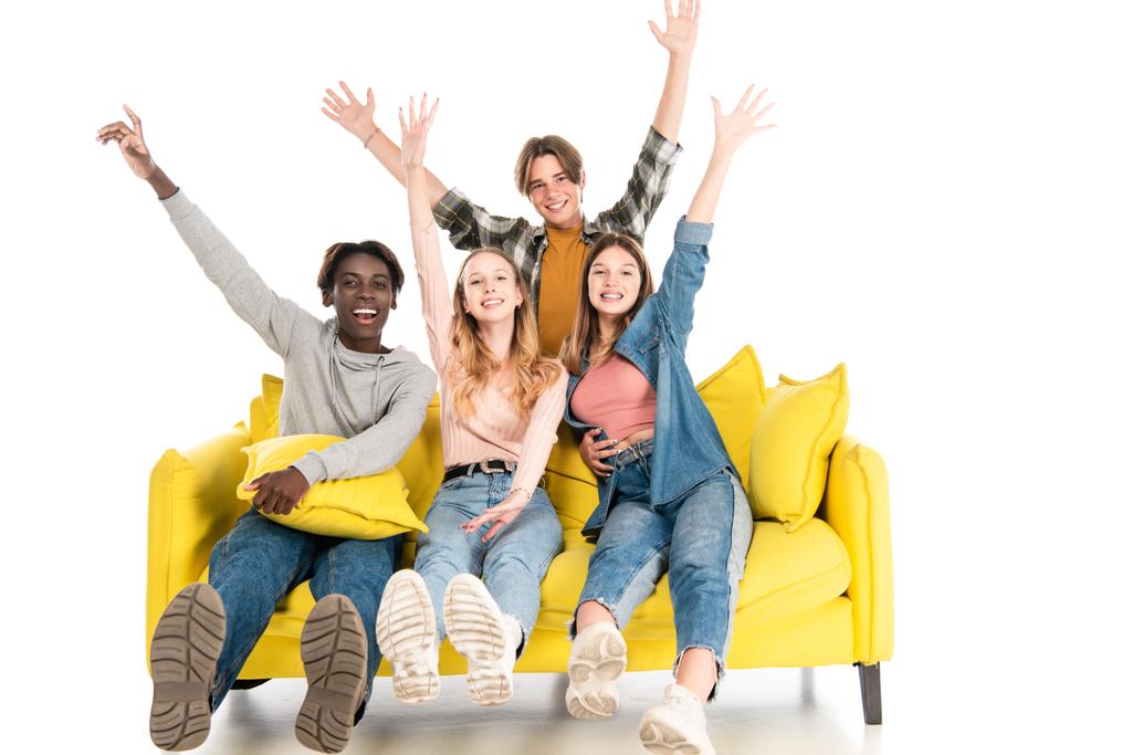 Adolescents multiculturels positifs agitant les mains et regardant la caméra sur le canapé sur fond blanc - Photo, image