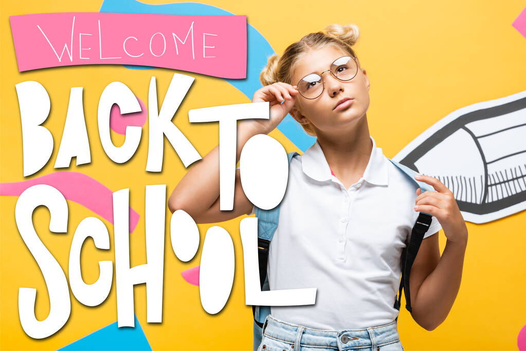 Nachdenkliche Schülerin berührt Brille in der Nähe von Bleistift, abstrakten Elementen und Willkommen zurück in der Schule Schriftzug auf gelb - Foto, Bild