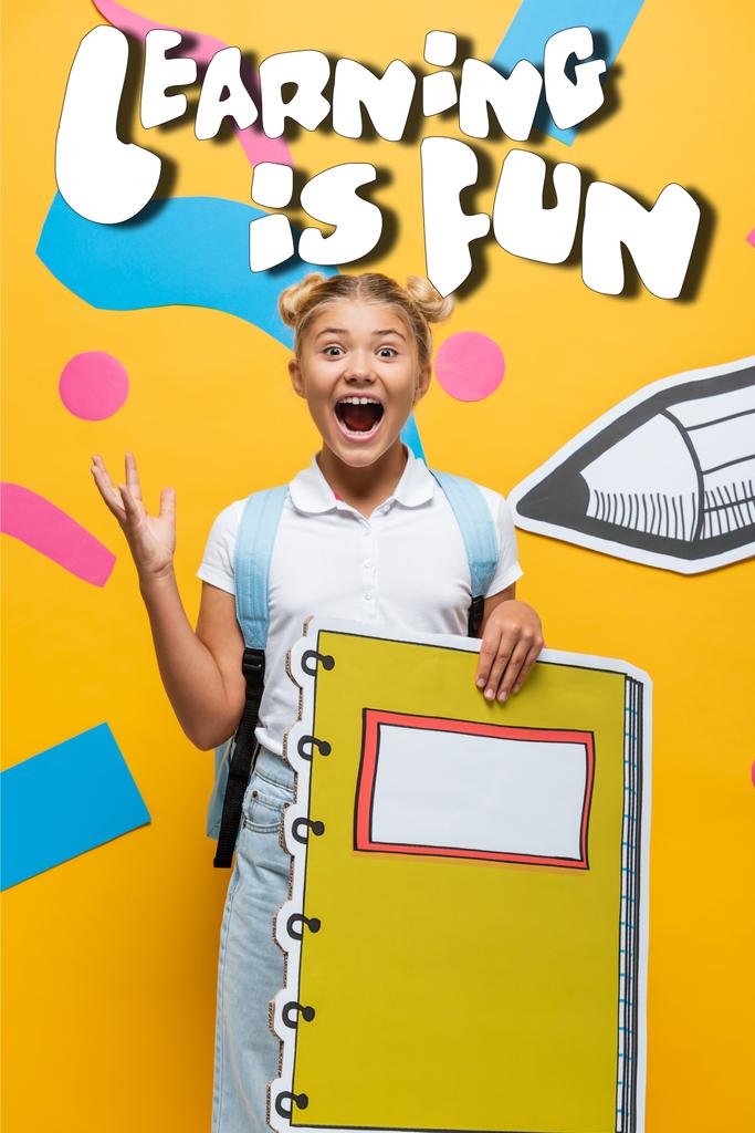 взволнованная школьница с блокнотом макет жесты рядом с декоративными элементами, обучение весело буквы и бумаги вырезать карандаш на желтый - Фото, изображение