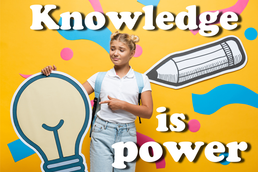 Écolière confus pointant avec le doigt à l'ampoule en papier près des éléments décoratifs et la connaissance est lettrage de puissance sur jaune  - Photo, image