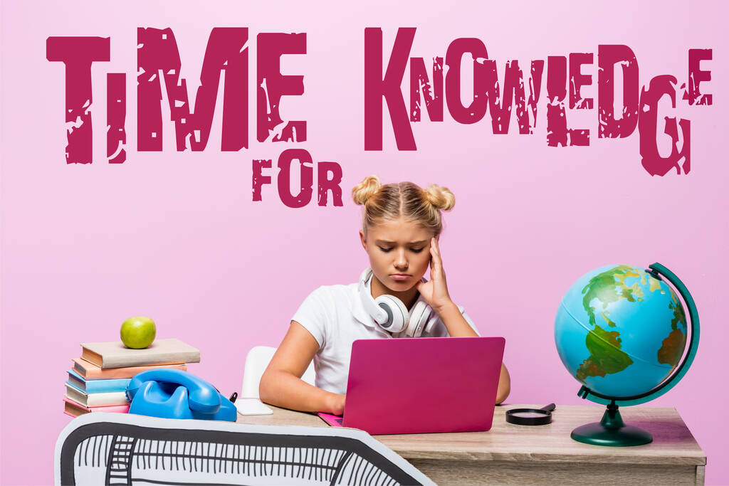 Triest kind in hoofdtelefoon met behulp van laptop in de buurt van de bol, boeken, retro telefoon, tijd voor kennis belettering en papier kunst op roze  - Foto, afbeelding