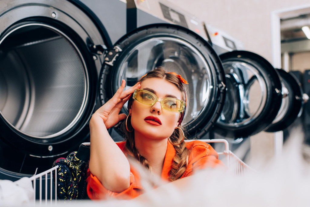 mulher pensativa perto de máquinas de lavar roupa com primeiro plano borrado - Foto, Imagem