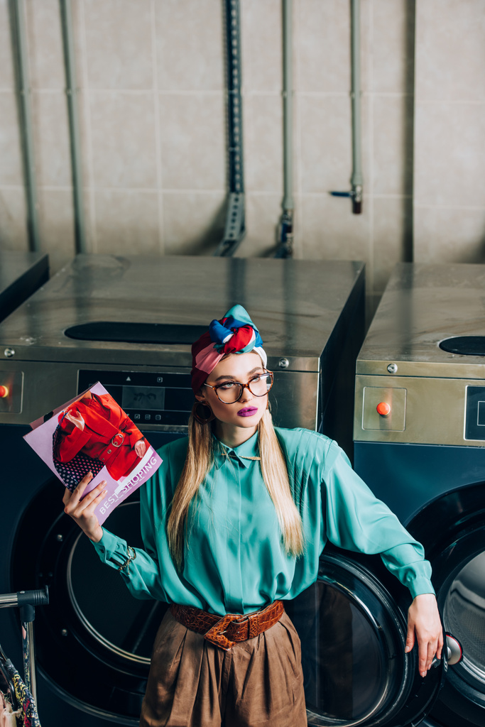 mujer joven y de moda en turbante y gafas celebración revista en lavandería  - Foto, imagen