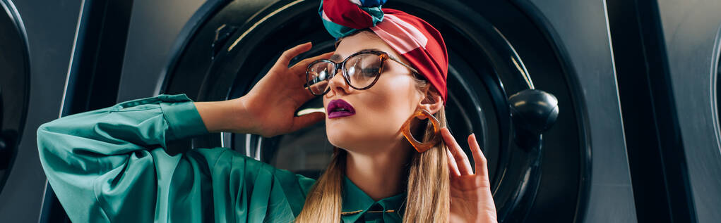 jovem elegante em óculos e turbante olhando para longe perto da máquina de lavar roupa, banner - Foto, Imagem