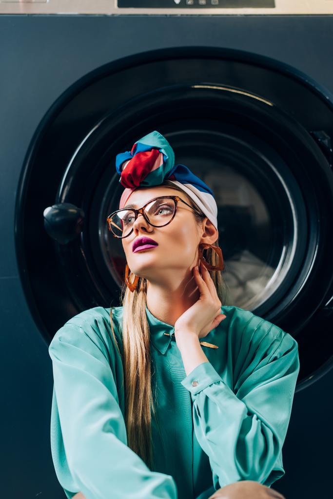 κομψή νεαρή γυναίκα με γυαλιά και τουρμπάνι σε πλυντήριο ρούχων - Φωτογραφία, εικόνα