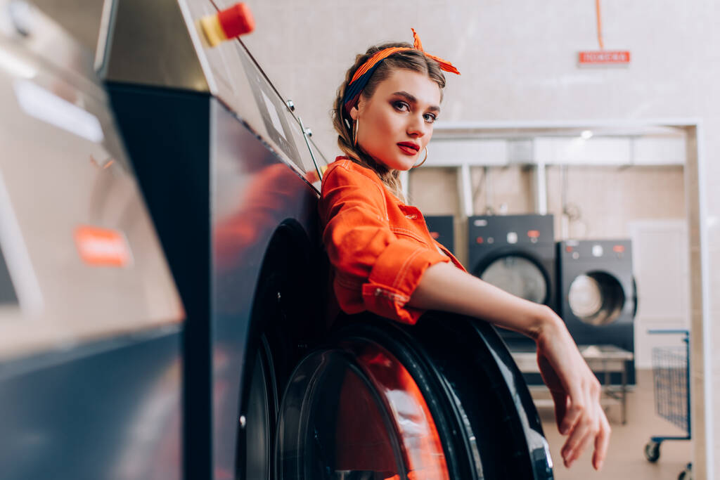 стильна жінка в обкладинці, дивлячись на камеру в сучасному пральні
  - Фото, зображення