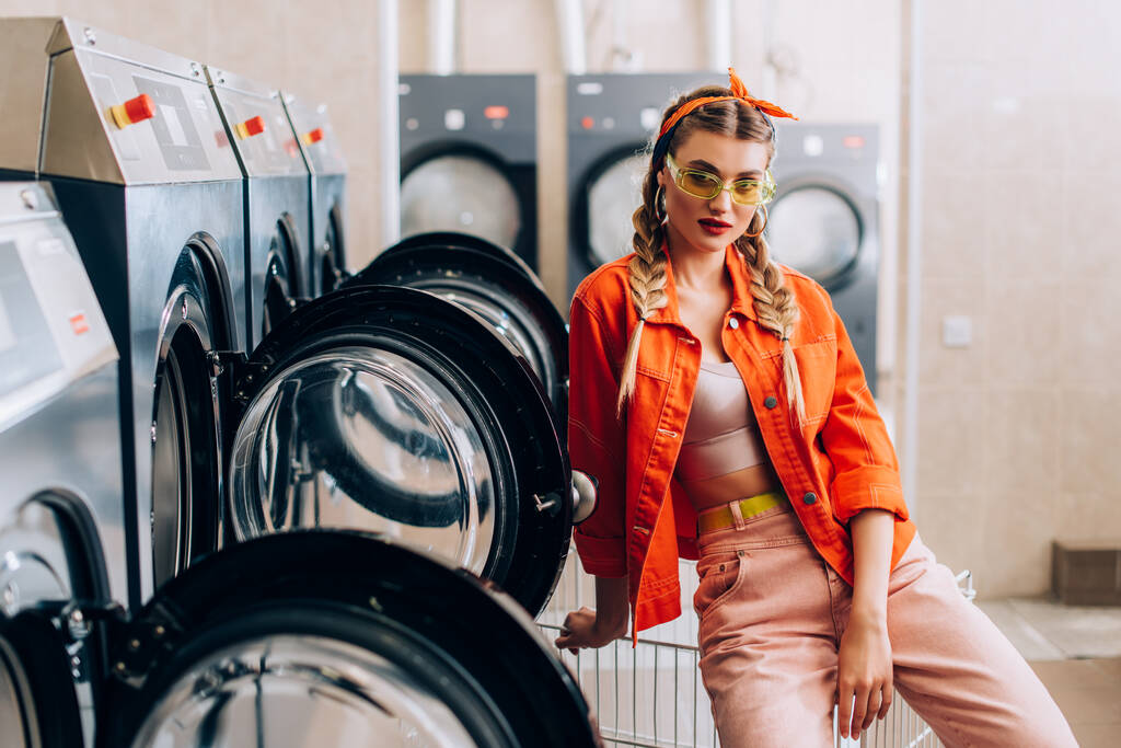 donna alla moda in fascia e occhiali da sole in lavanderia moderna  - Foto, immagini