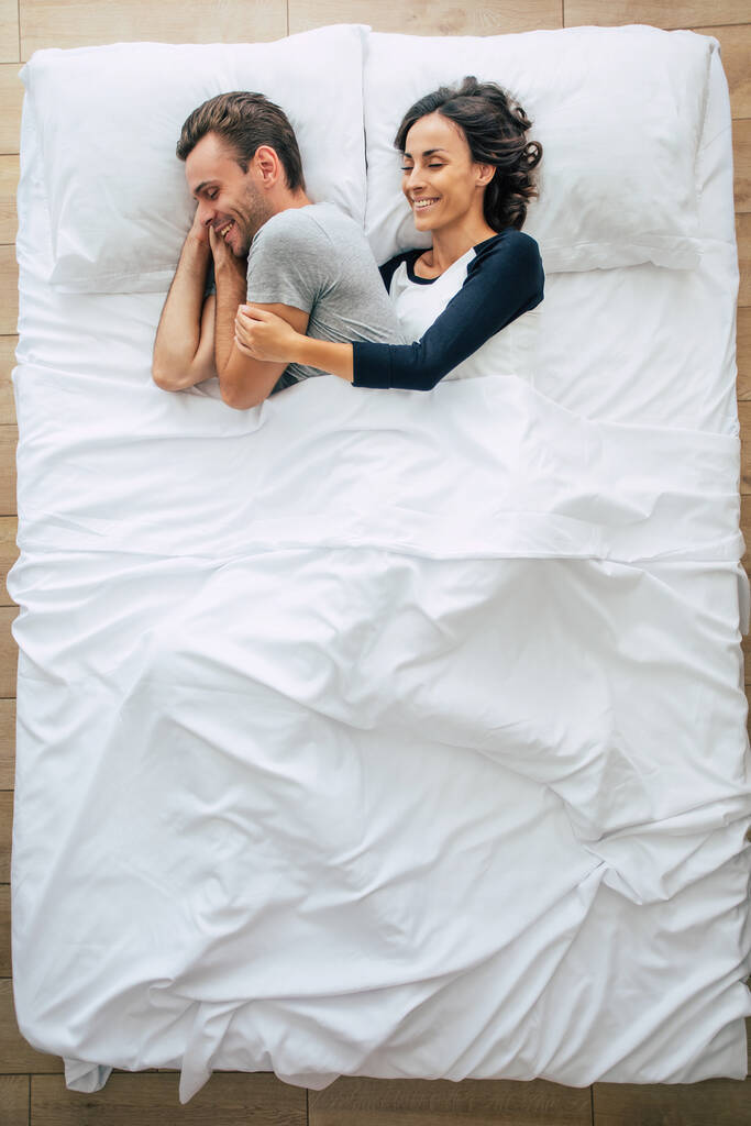 Hora de dormir. La familia está durmiendo. Hermosa pareja joven en el amor están acostados en la gran cama blanca y descansando. Esposo y esposa juntos en la cama. Vista superior foto - Foto, imagen