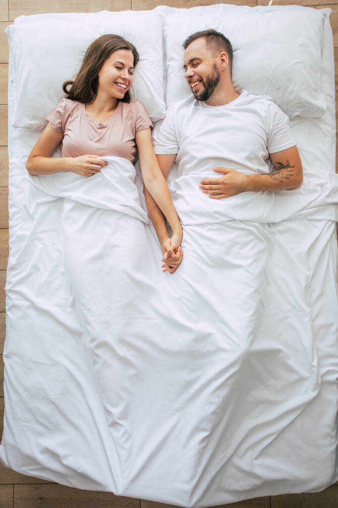 Bedtijd. De familie slaapt. Mooi jong verliefd echtpaar liggen op het grote witte bed en rusten uit. Man en vrouw samen in bed. Bovenaanzicht foto - Foto, afbeelding