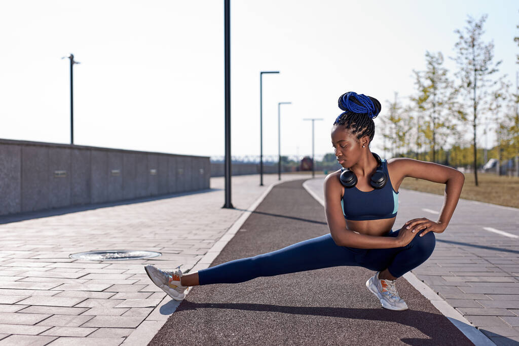 спортсмен афро-жінка розтягує м'язи ноги під час тренування на відкритому повітрі
 - Фото, зображення