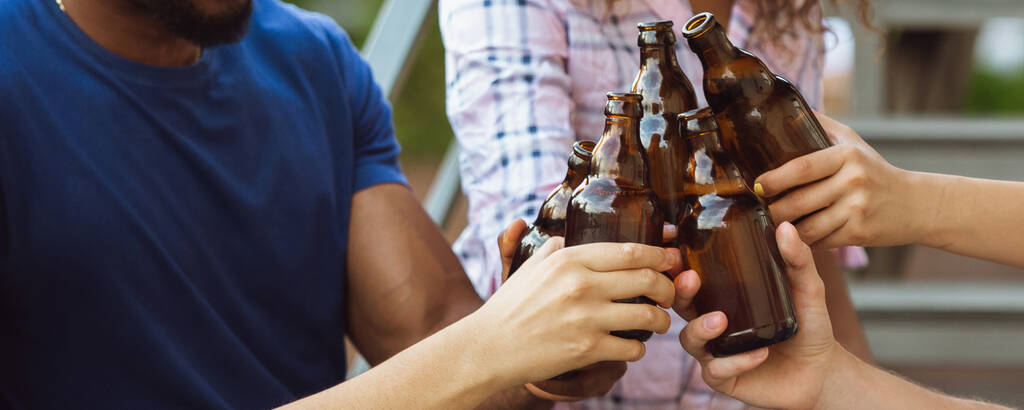Manos de jóvenes amigos, colegas bebiendo cerveza, divirtiéndose, riéndose y celebrando juntos. Folleto con copyspace - Foto, imagen